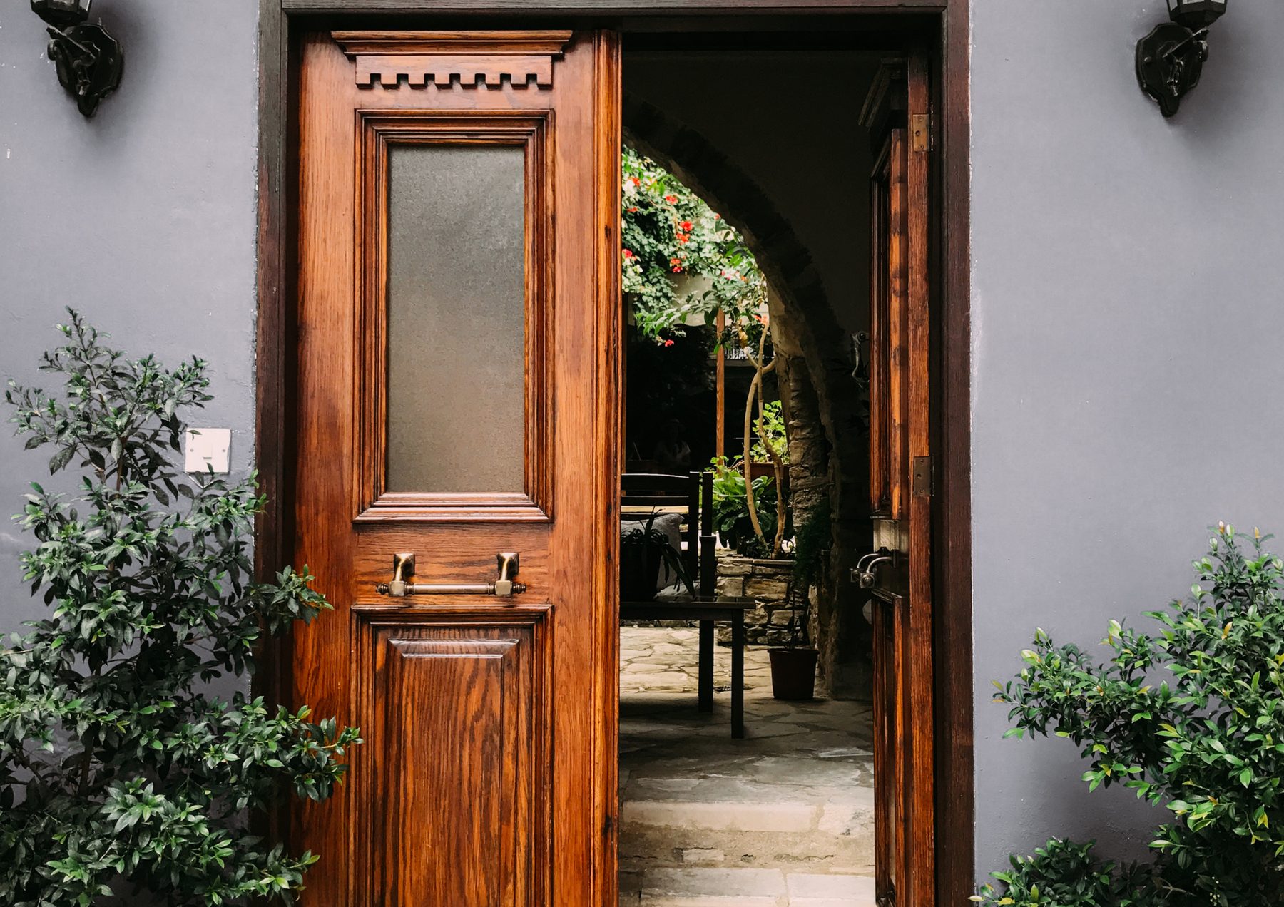 A dark ornate wooden door standing open onto a quiet courtyard